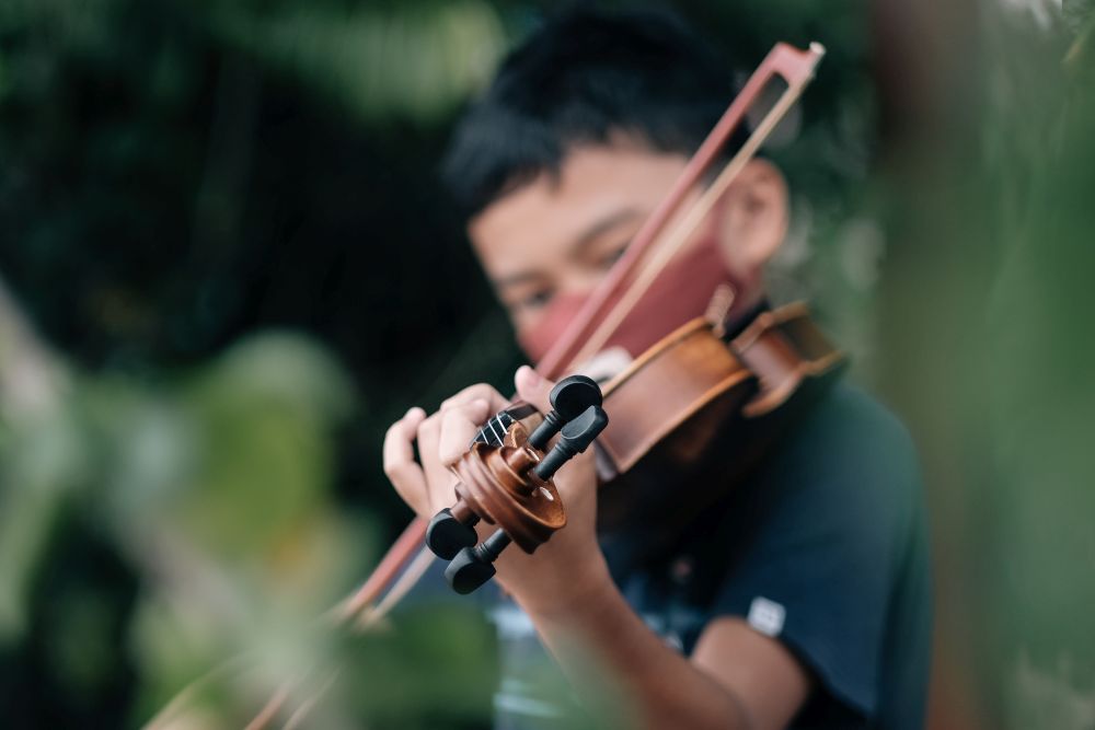 A person plays a violin outdoors, with green foliage in the blurred background—capturing the spirit of violin lessons Singapore enthusiasts enjoy.